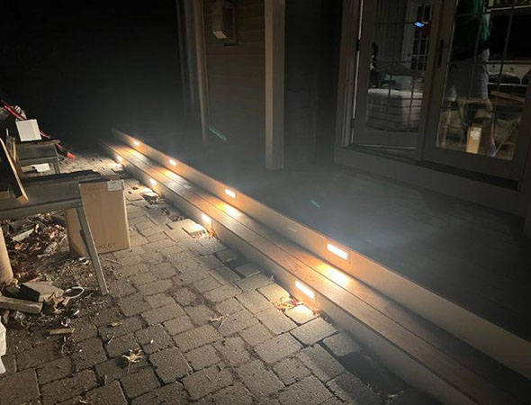 Well-lit outdoor steps at night, featuring modern lighting along the sides, with scattered debris and a few outdoor items nearby.